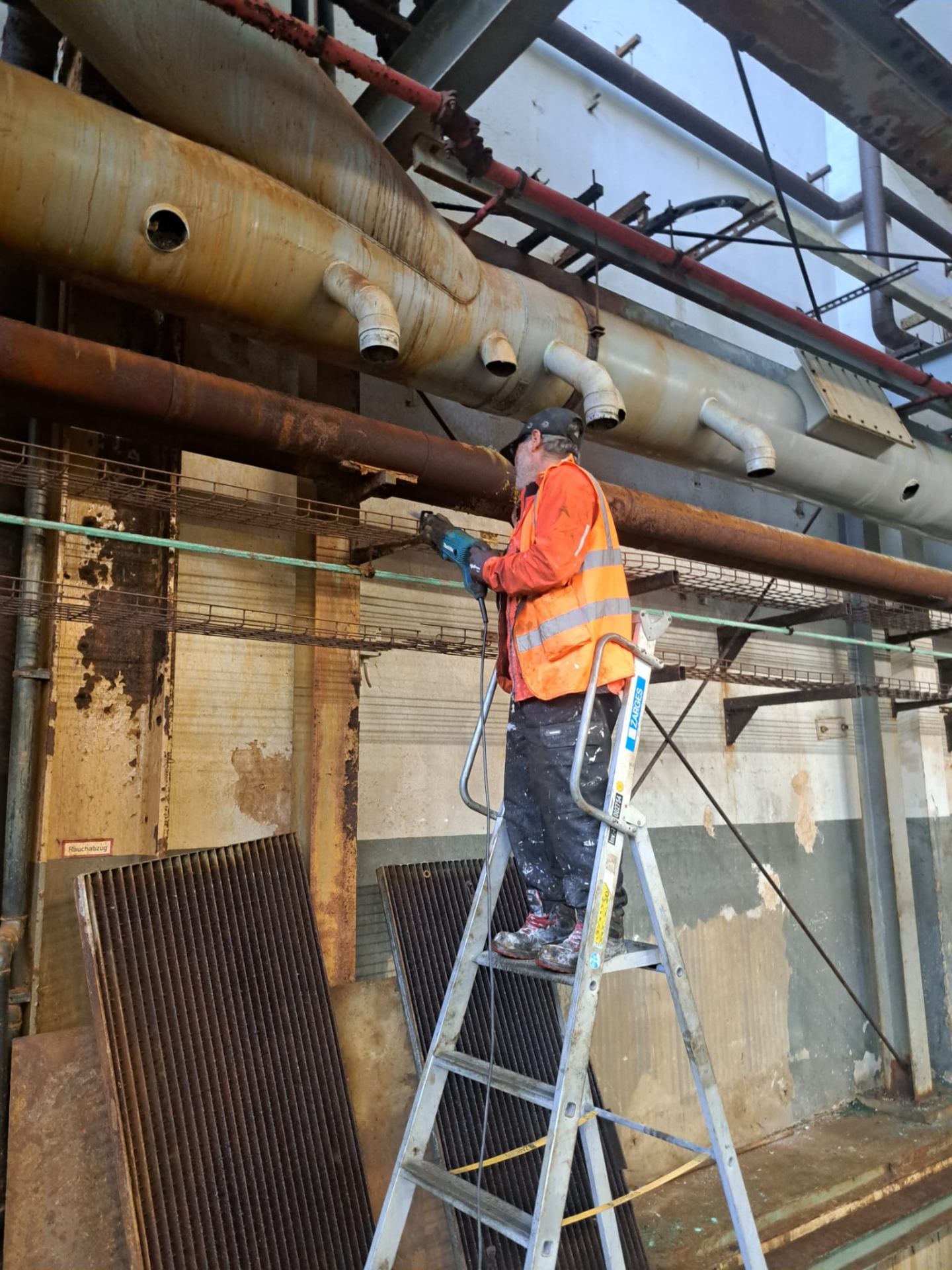 Monteur demontiert mit Säbelsäge Rohrleitungen und Infrastruktur in einer Industriehalle